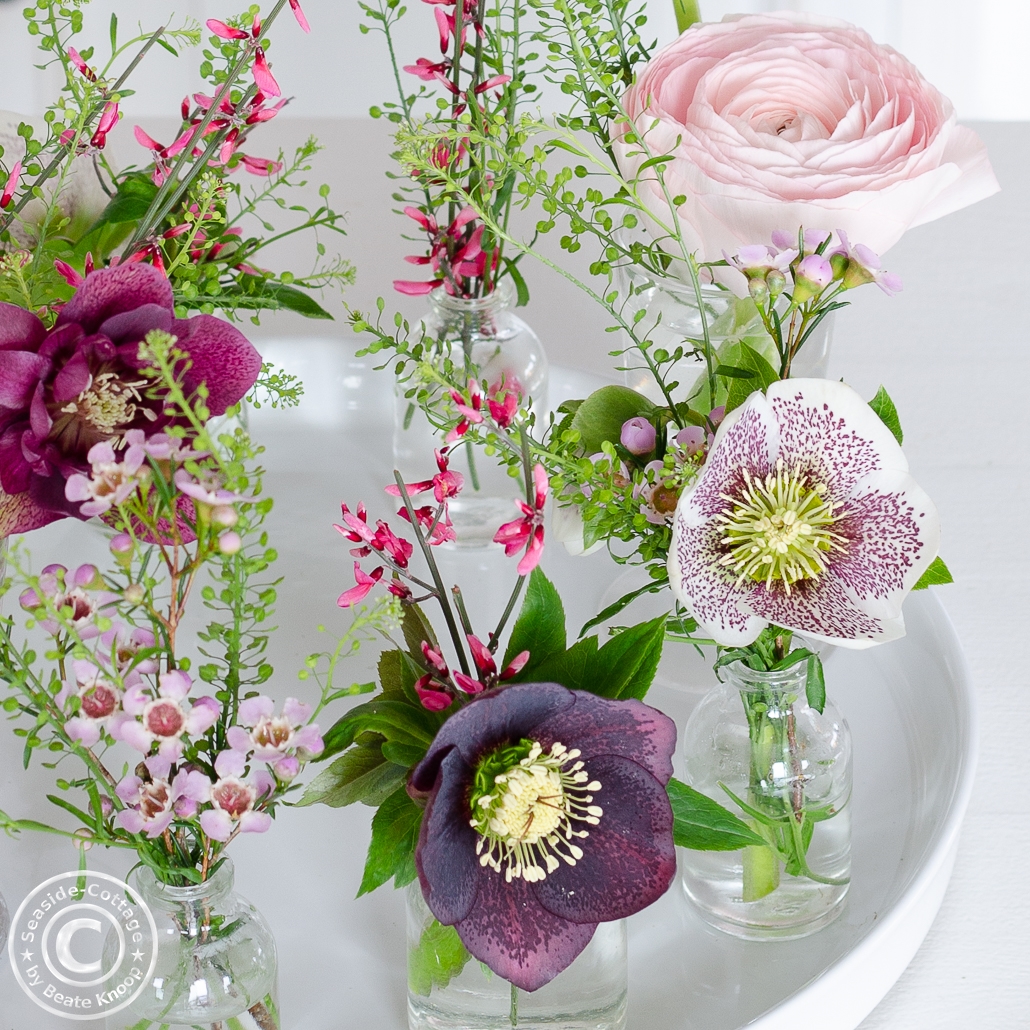 Blumendeko mit Ranunkeln und Lenzrosen in kleinen Vasen