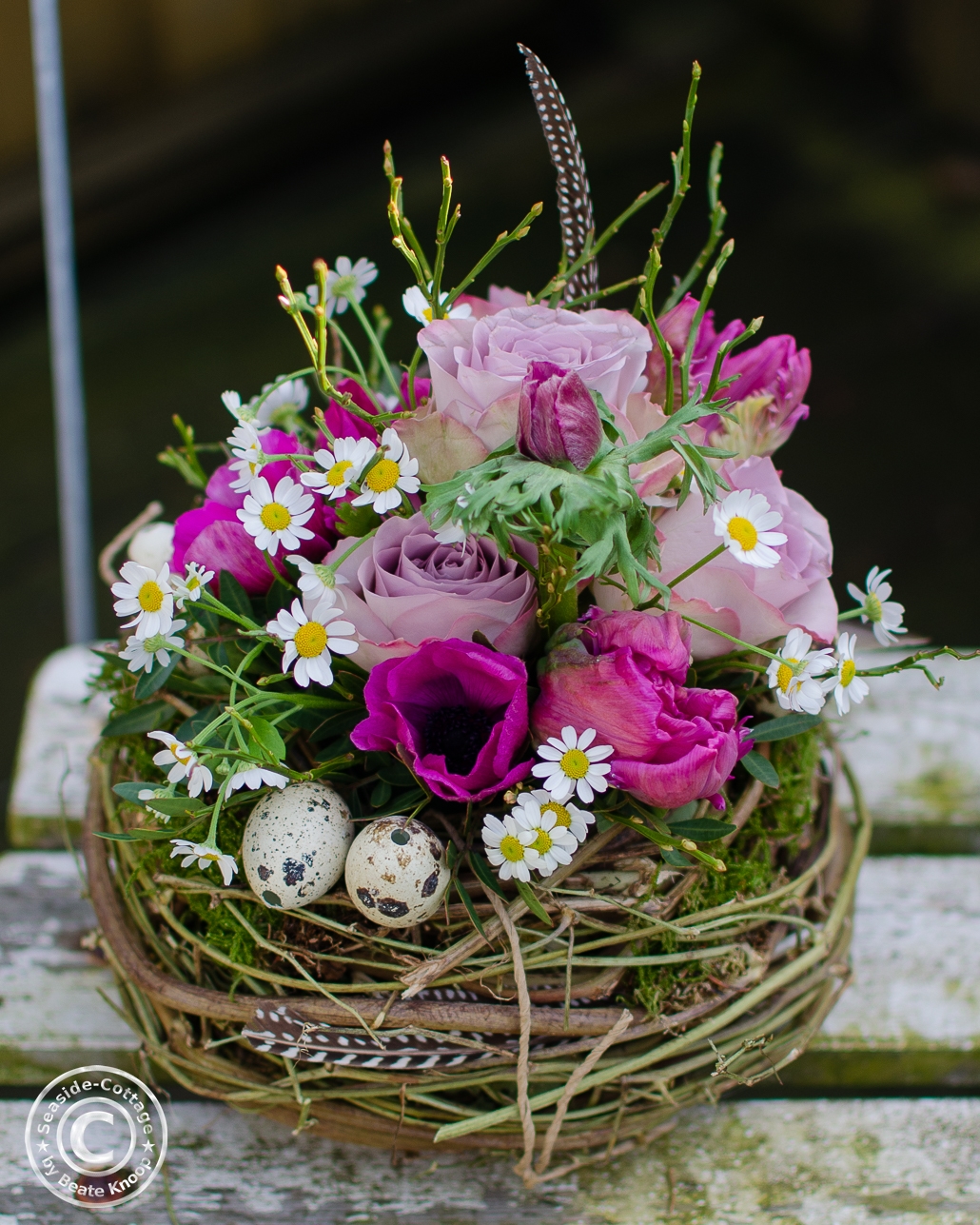 Nest aus Hopfenrebe geüllt mit pinkfarbenen Anemonen und Tulpen, fliederfrabenen Rosen, Edelkamille, Heildebeergrün und Wachteleiern