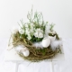 Osternest in Weiß mit Hornveilchen bepflnazt und mit Gänseeiern und Federn dekoriert auf einem alten weißen Holzhocker