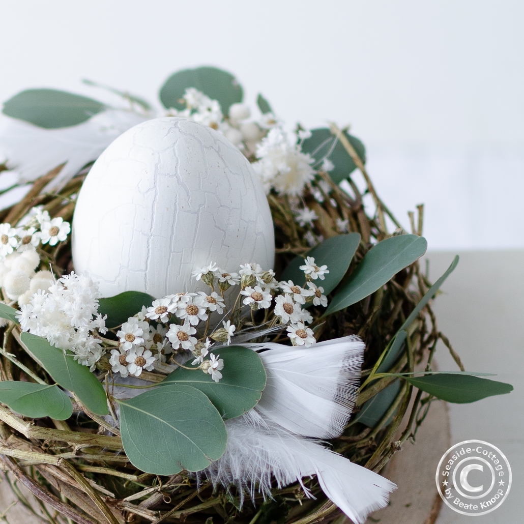 Weißes Ei in einem Nest mit Trockenblumen und Federn dekoriert