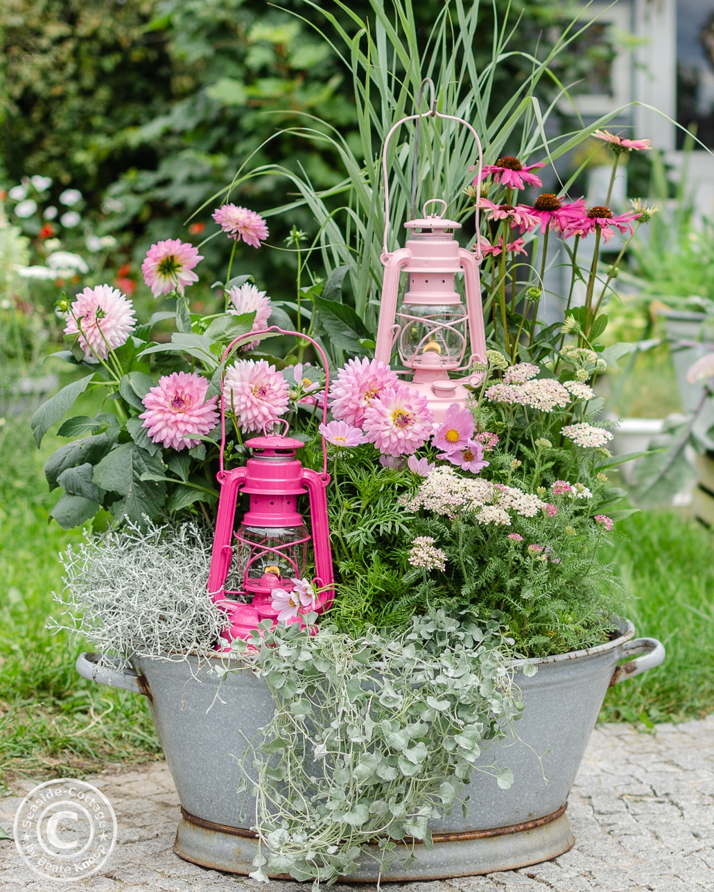 Gartendeko mit zwei Laternen in Rosa und Pink der Marke Feuerhand Baby Special, eindekoriert in einer sommerlich bepflanzten Zinkwanne mit rosa Blumen