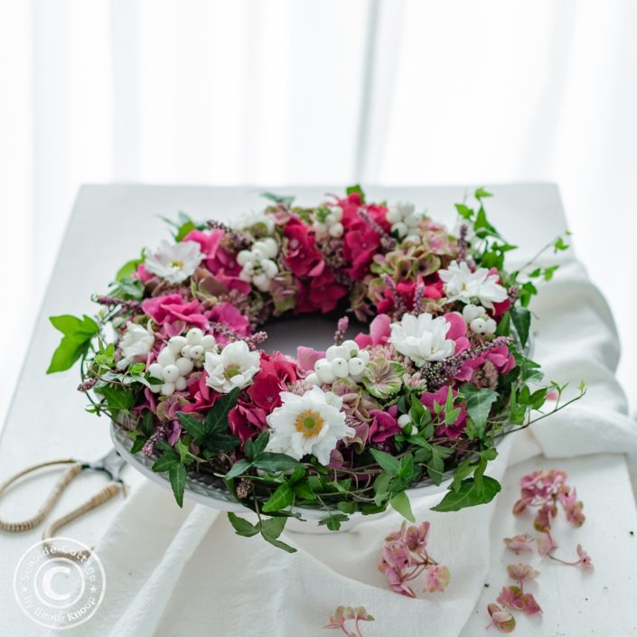 diy-anleitung-gesteckter-herbstkranz-mit-hortensien 03 rosa Hortensienkranz mit Herbstanemonen auf Tisch mit weißer Tischdecke vor einem Fenster mit weißer Gardine