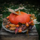 Herbstdeko: Großer oranger Kürbis auf Korbtablett, dekoriert mit Herbstlaub, Ziermais und Physalis
