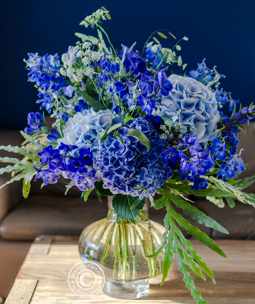 Strauß mit blauem Rittersporn und blauen Hortensien vor blauer Wand